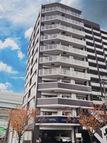Un hotel de varios pisos con balcones, un letrero que indica 'HOTEL' y un árbol con hojas otoñales al frente.