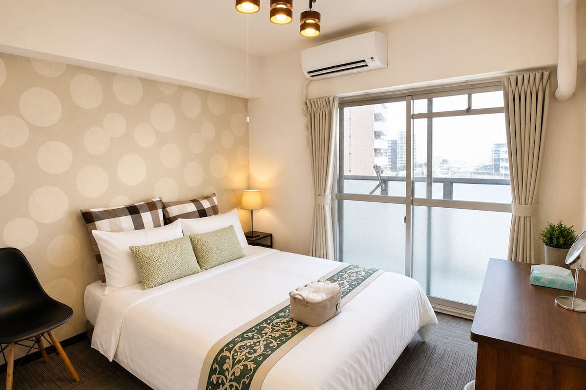 Habitación de hotel con cama, una silla, escritorio, aire acondicionado y ventana con cortinas.