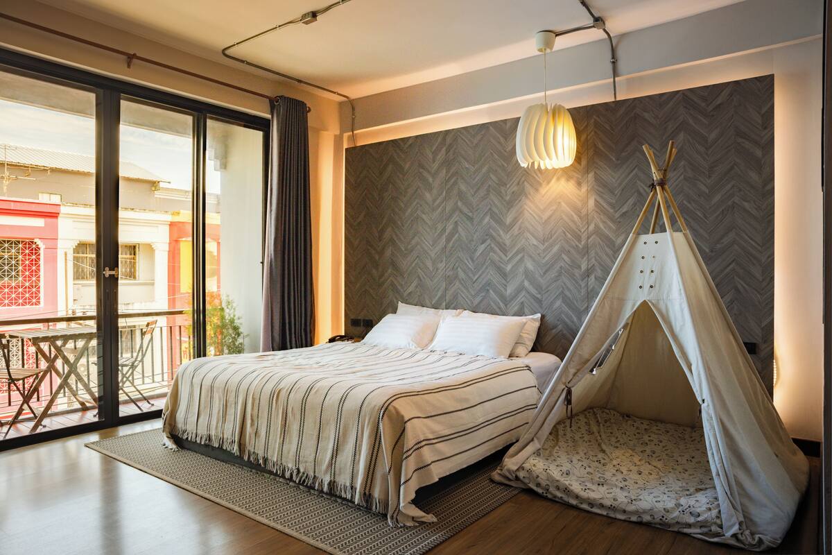 A bedroom with a bed, a large window, a balcony, and a teepee.