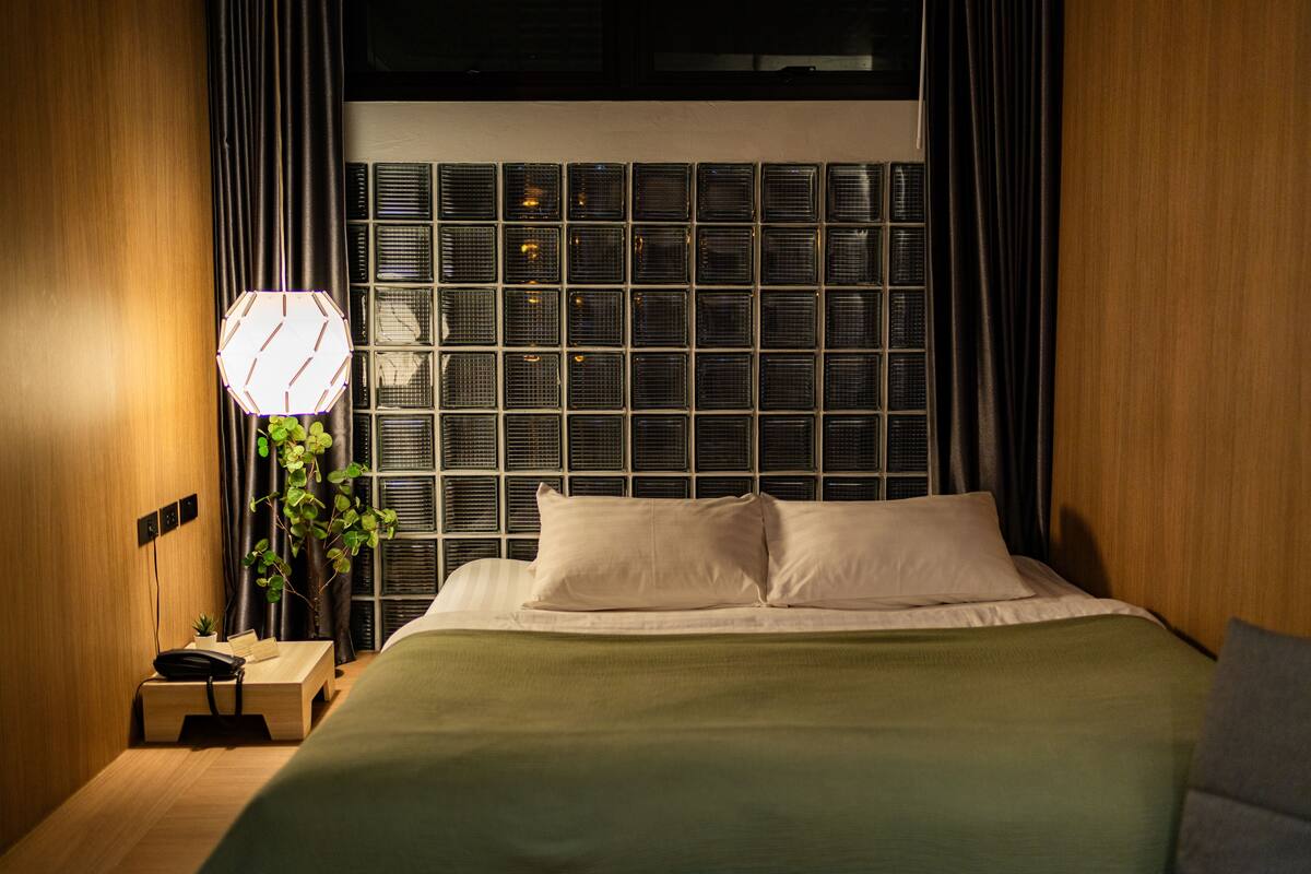 A neatly made bed with white linens, a bedside table with a lamp, and a plant.