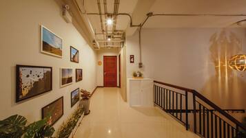 A hallway with a wooden door, a staircase with a black railing, and several framed pictures on the walls.