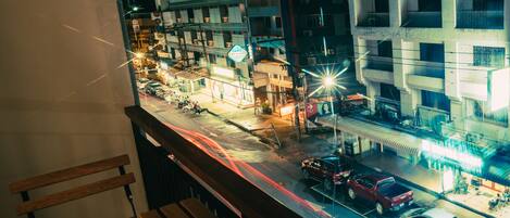 Vista nocturna de la calle desde un balcón, con un camino transitado, edificios y una estación de servicio.