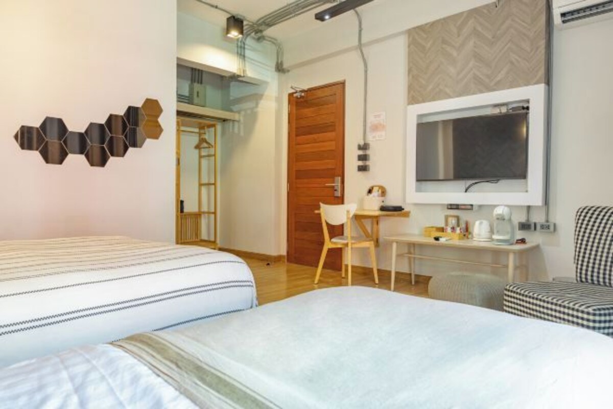 A hotel room with two beds, a desk with a chair, a large mirror, and a wardrobe.