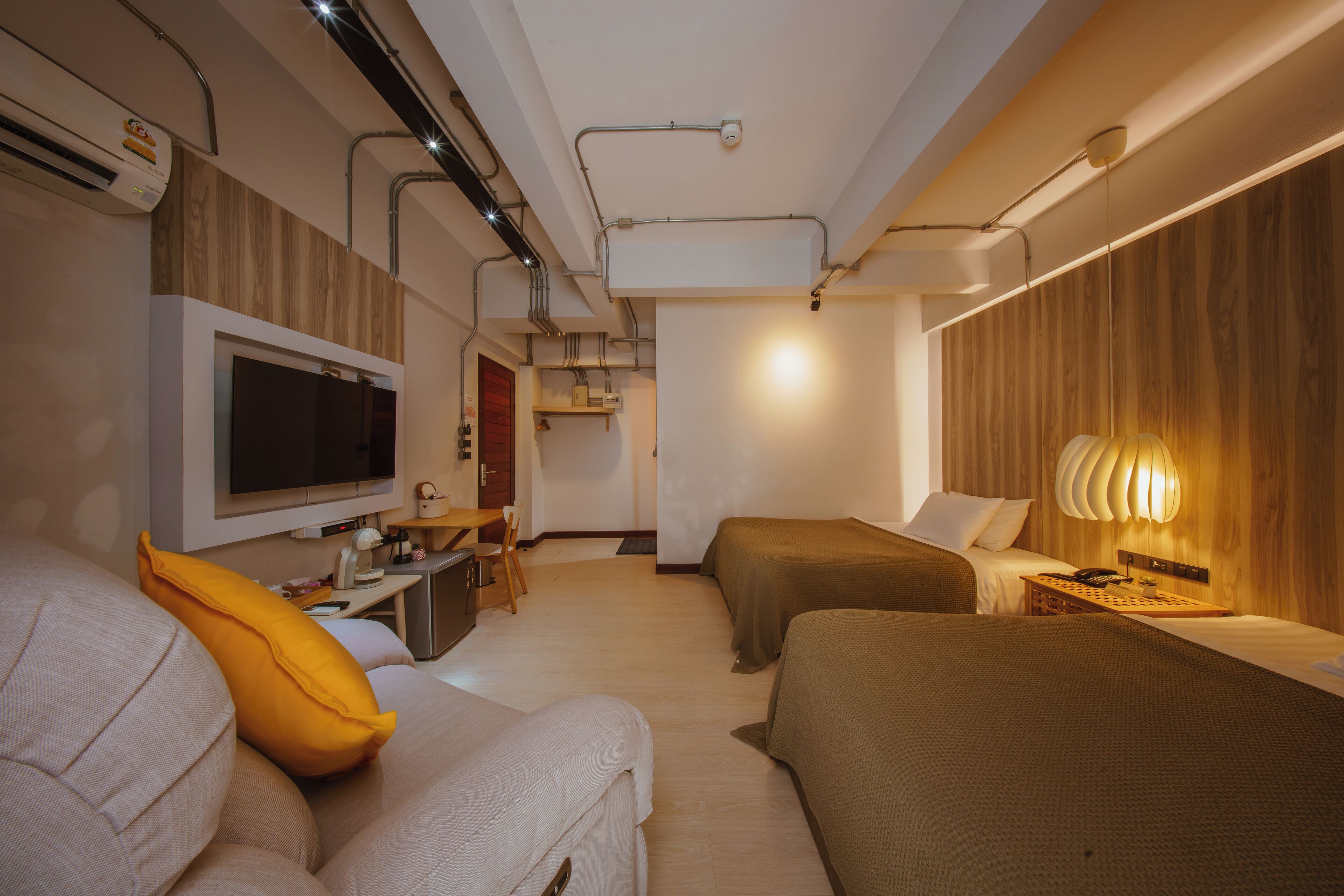 A modern hotel room with a flat-screen TV, two beds, a desk with a chair, and a lamp.
