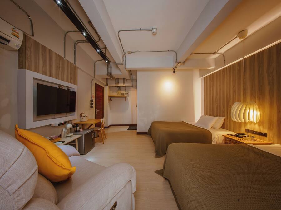 Habitación de hotel moderna con una televisión de pantalla plana, dos camas, un escritorio con silla y una lámpara.