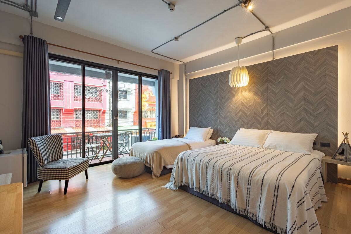 A modern bedroom with a large bed, a chair, and a balcony with a red building view.