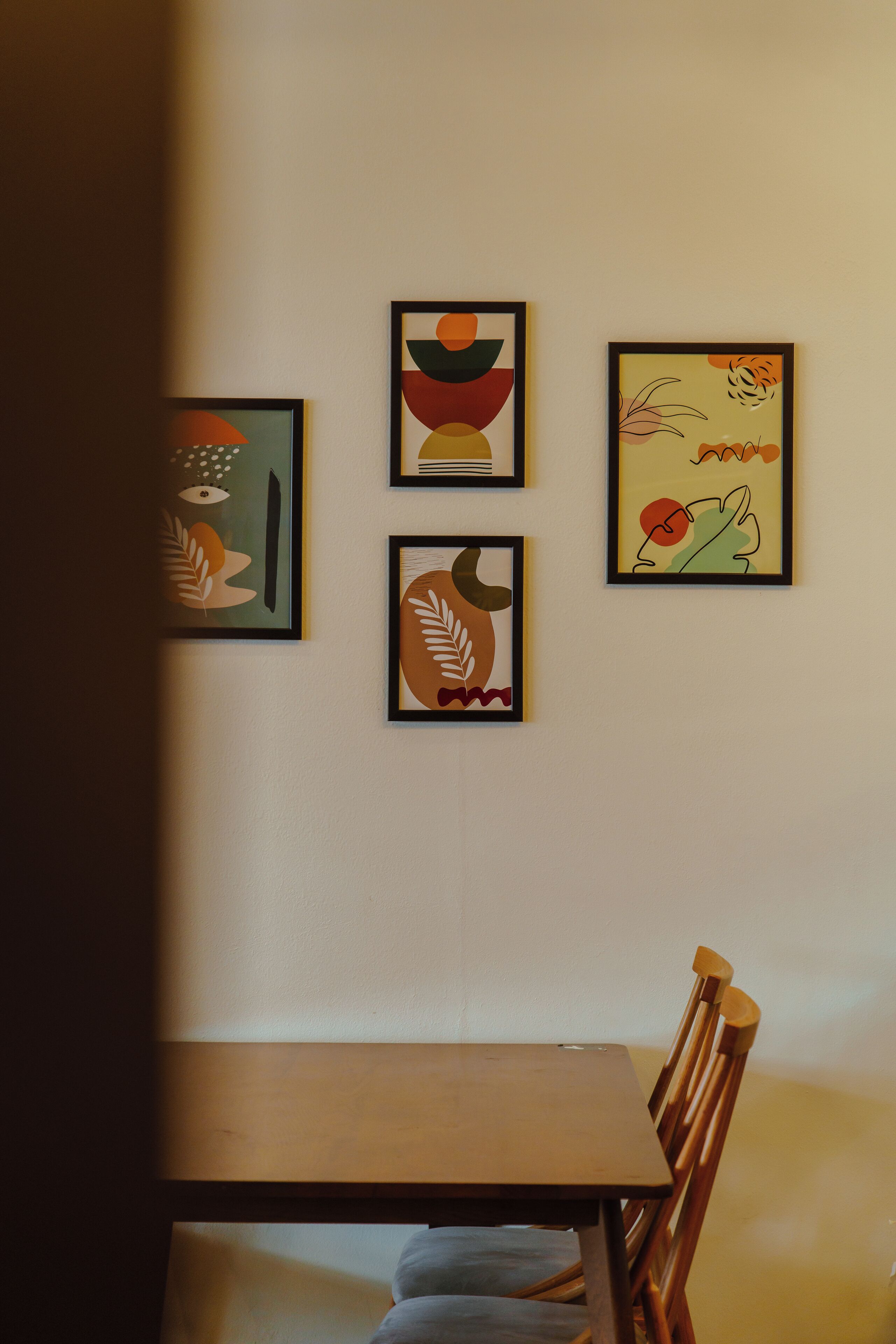 A dining area with a wooden table and chairs, and four framed artworks on the wall.