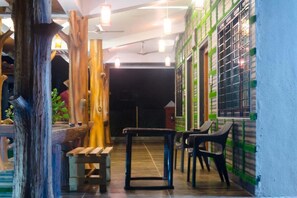 A corridor with wooden pillars, a bench, and a table with chairs. - Malhar Villa (Murud)