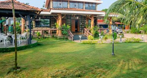 A two-story building with a covered patio area, outdoor seating, and a well-maintained lawn. - Malhar Villa (Murud)