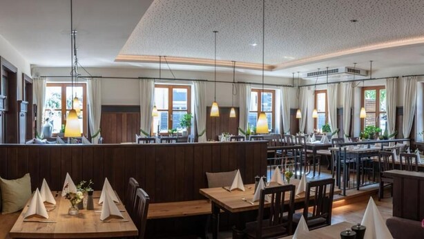Un restaurant doté de plusieurs espaces de restauration, de meubles en bois et d’un éclairage suspendu.