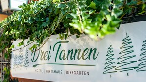 Une enseigne pour le « Wirtshaus Biergarten », ornée d’une décoration représentant une vigne verte.