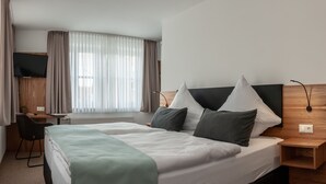 Une chambre d’hôtel avec un lit, un bureau, une chaise, une télévision et une fenêtre avec des rideaux.