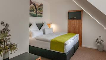 A bedroom with a bed, a painting of a bridge, a TV, and a plant.