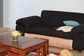 A living room with a black sofa, a wooden coffee table, and a vase of flowers. - Homeabroad Ensuite Apartment (Dar es Salaam)