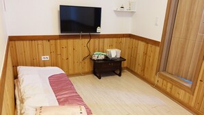 Un dormitorio con cama, televisión en la pared, una mesita con objetos y paneles de madera.