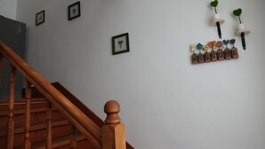 Una escalera de madera con barandillas y pasamanos, que conduce a un rellano con una pared blanca. Se observan cuadros enmarcados y un letrero decorativo que dice 'WELCOME' con pequeños adornos con forma de casa.
