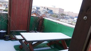 Una mesa de madera cubierta de nieve, un techo verde y una vista de edificios al fondo.