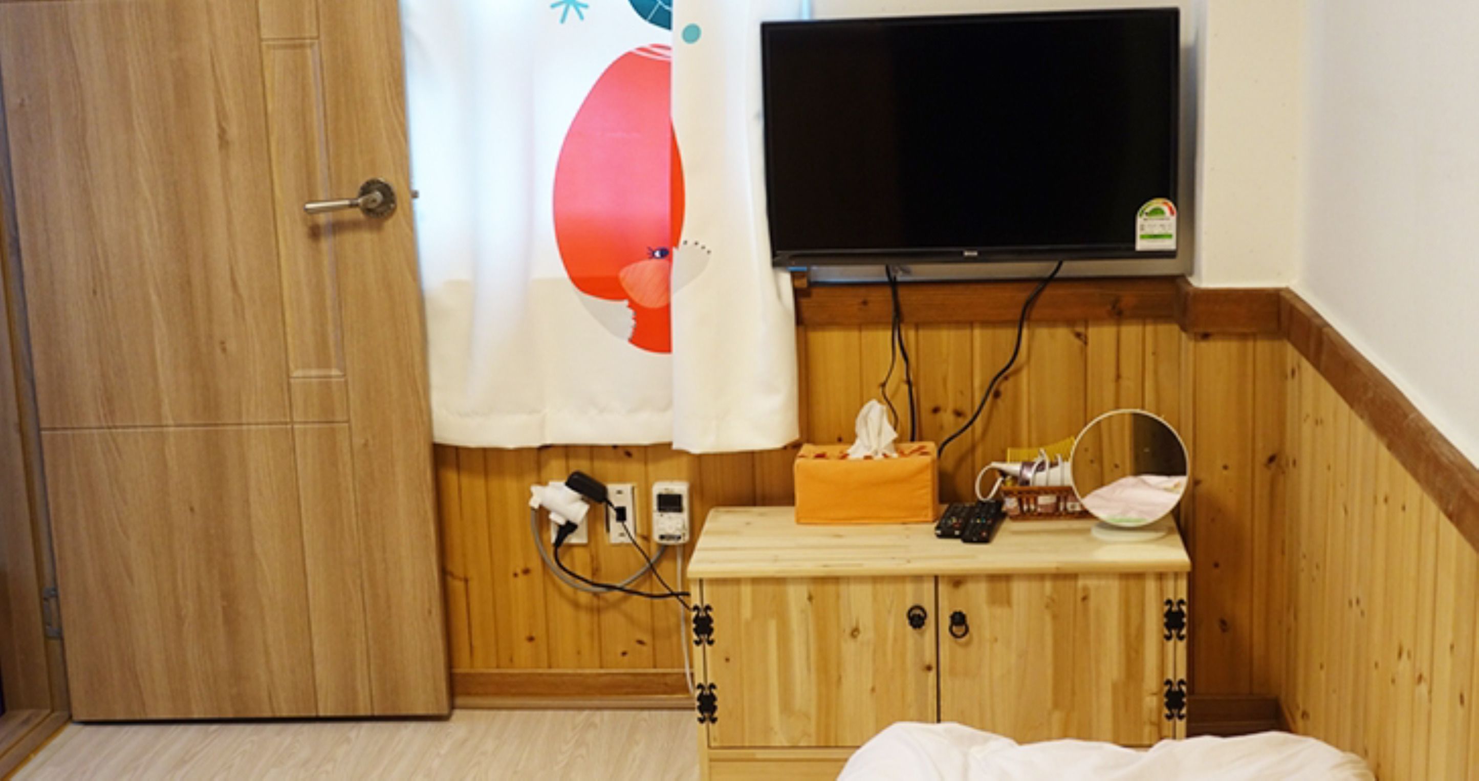 Un meuble en bois sur lequel est fixée une télévision, une table de chevet avec une boîte de mouchoirs et un miroir.