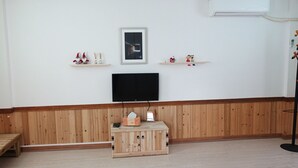 Una habitación con un banco de madera, un televisor sobre un soporte y dos estanterías con objetos decorativos.