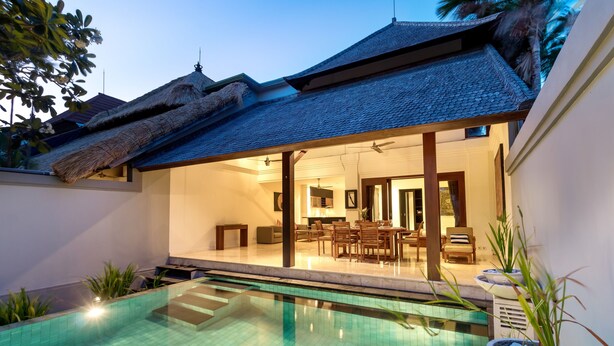 A modern pool area with a clear pool, a dining area with chairs and a table, and a thatched roof structure. - Villa Lalang Temu (Jimbaran)