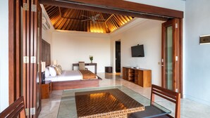 A modern bedroom with a glass coffee table, wooden furniture, a ceiling fan, and a TV on the wall. - Villa Lalang Temu (Jimbaran)
