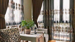 A living room with a sofa, a coffee table with a plant and a bottle, and a view through sheer curtains. - F&F Hotel (Hai Phong)