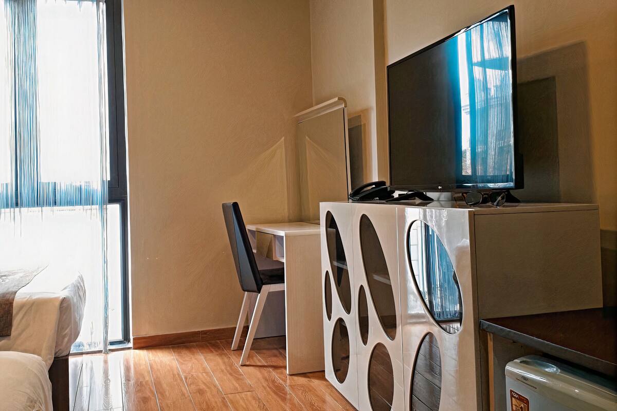 Ein kompakter Wohnbereich mit Bett, Schreibtisch, Fernseher und Kühlschrank.