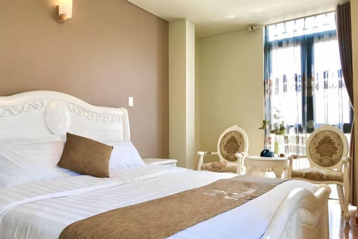 Habitación de hotel con una cama grande, dos sillas, una mesita y una ventana con cortinas.