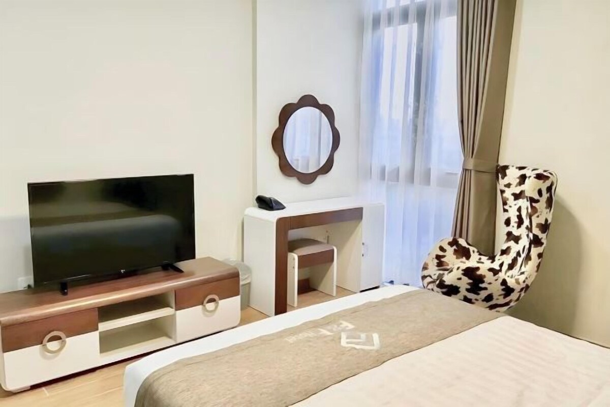 A hotel room with a bed, a TV, a desk, a chair, and a mirror.