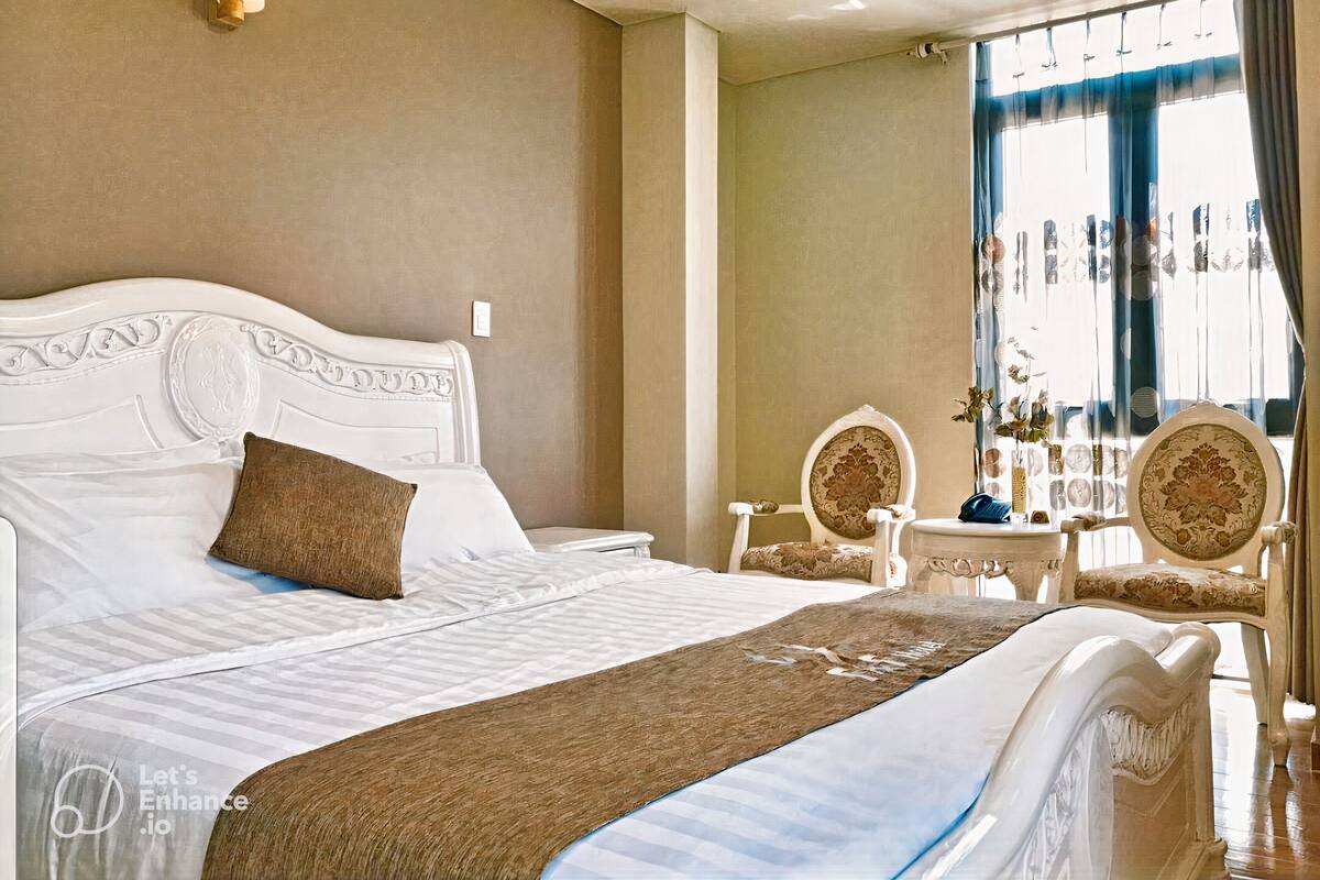 Ein Hotelzimmer mit einem großen Bett, zwei Sesseln, einem kleinen Tisch und einem Fenster mit Vorhängen.
