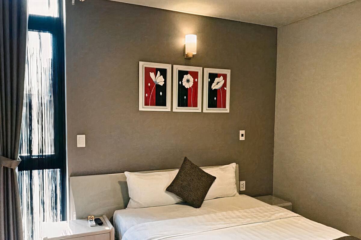 Ein Hotelzimmer mit einem Bett, einem Nachttisch, einer Wandleuchte und drei gerahmten Blumenbildern.