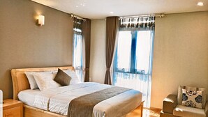 A neatly made bed with a wooden frame, a bedside table, and a chair with patterned cushions. - F&F Hotel (Hai Phong)