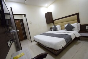 A hotel room with a bed, a desk, a chair, a TV, and a wardrobe. - The Lake Palace (Ahmedabad)