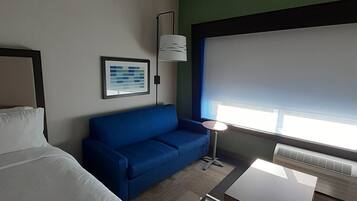 Une chambre d’hôtel avec un lit, un canapé bleu, une petite table, un lampadaire et une grande fenêtre.