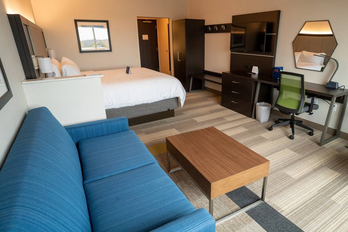 A hotel room with a bed, a desk with a chair, a small table, a sofa, and a TV.