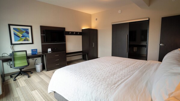 A hotel room with a bed, desk, chair, wardrobe, and a television.