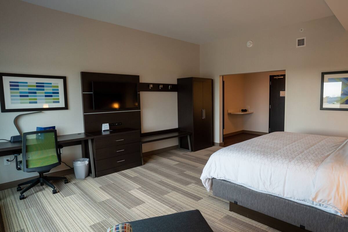 A hotel room with a bed, a desk with a computer, a TV, and a wardrobe.