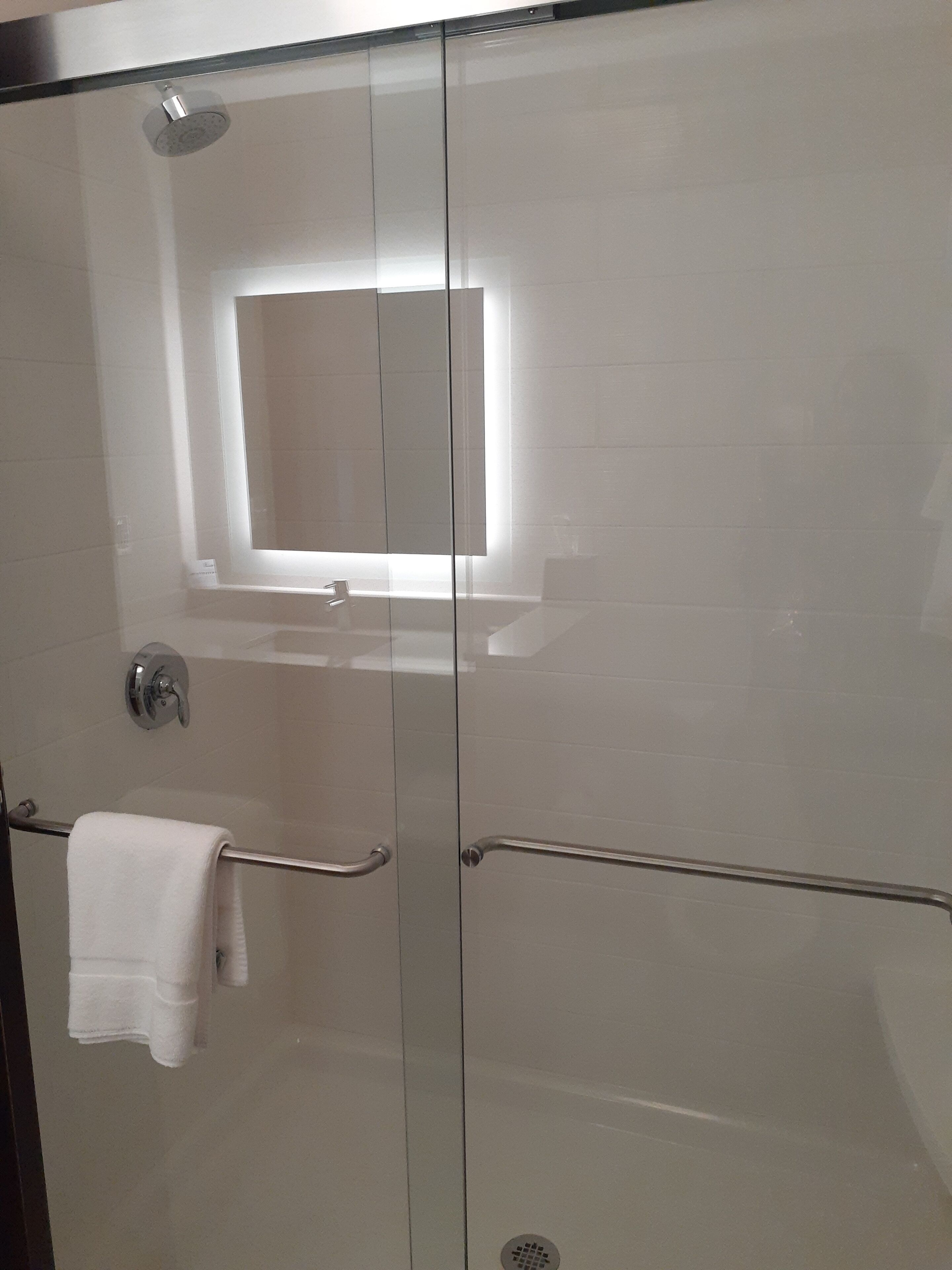 A glass-enclosed shower with a white towel hanging on a metal handle.