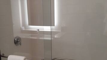 A glass-enclosed shower with a white towel hanging on a metal handle.