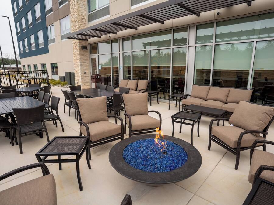 Un patio al aire libre con arreglos de asientos, una chimenea y un edificio con grandes ventanales al fondo.