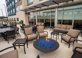 Un patio al aire libre con arreglos de asientos, una chimenea y un edificio con grandes ventanales al fondo.