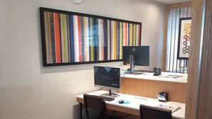 A small office space with a desk, two chairs, a computer, and a monitor. There is a framed artwork on the wall and a window with blinds. - Holiday Inn Express Richburg by IHG (Richburg)