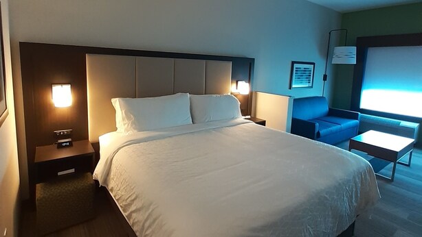 A hotel room with a large bed, bedside tables, a nightstand, a blue sofa, and a small table. - Holiday Inn Express Richburg by IHG (Richburg)