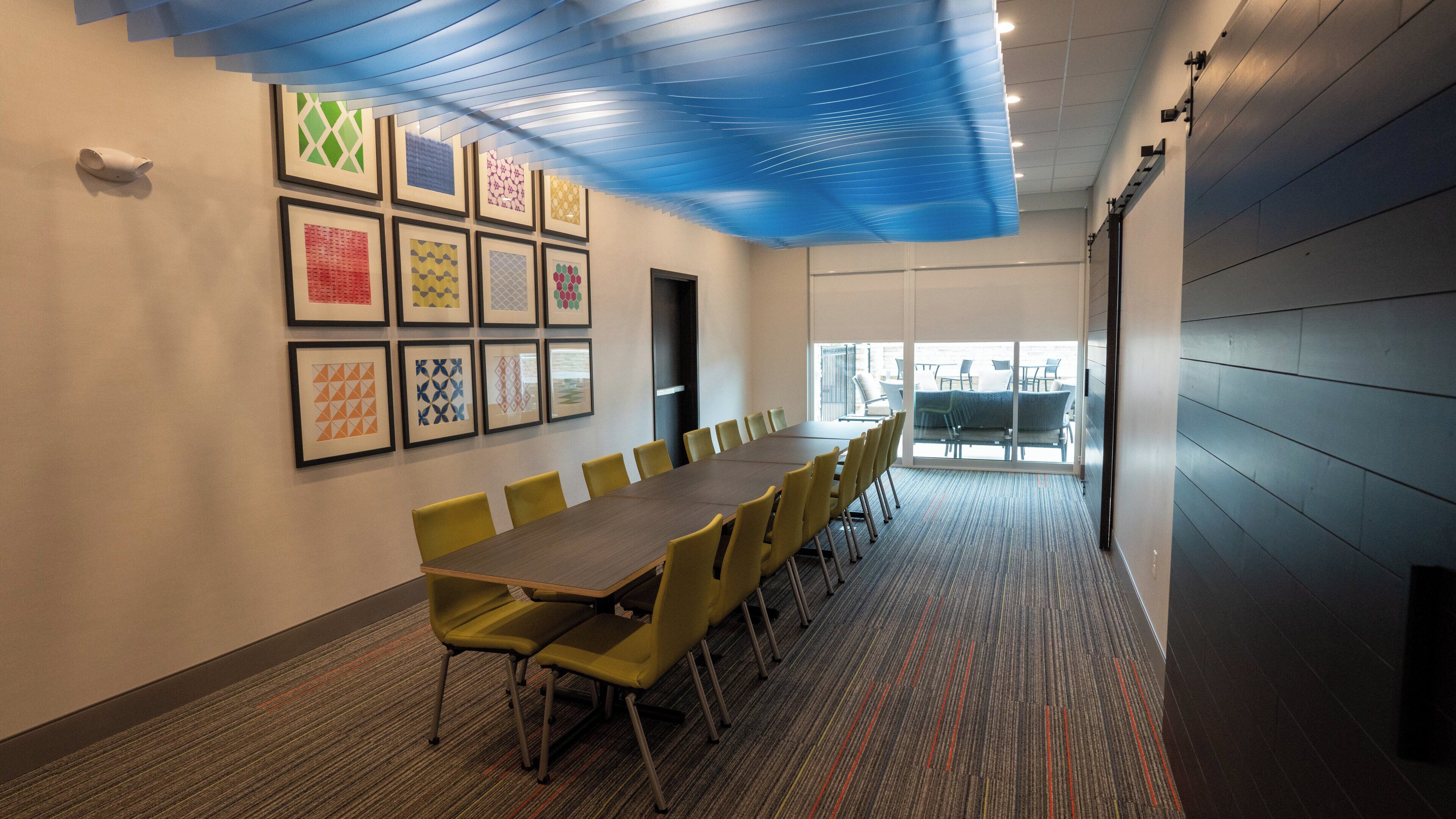 Un salón de conferencias con una larga mesa, sillas amarillas y cuadros decorativos en la pared.