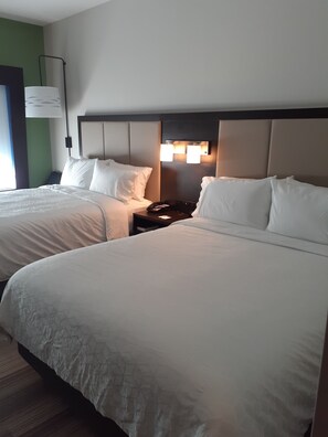 A hotel room with two beds, a nightstand with a phone and lamp, and a wall-mounted light fixture.