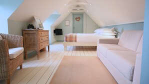 A bedroom with a sloped ceiling, a bed with a heart-shaped decoration, a wicker chair, a wooden dresser, and a light-colored sofa. - The Apartments Quidhampton Mill (Salisbury)