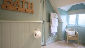A bathroom with a wooden sign reading "BATH", a towel rack with towels, a wicker chair, and a toilet paper holder. - The Apartments Quidhampton Mill (Salisbury)