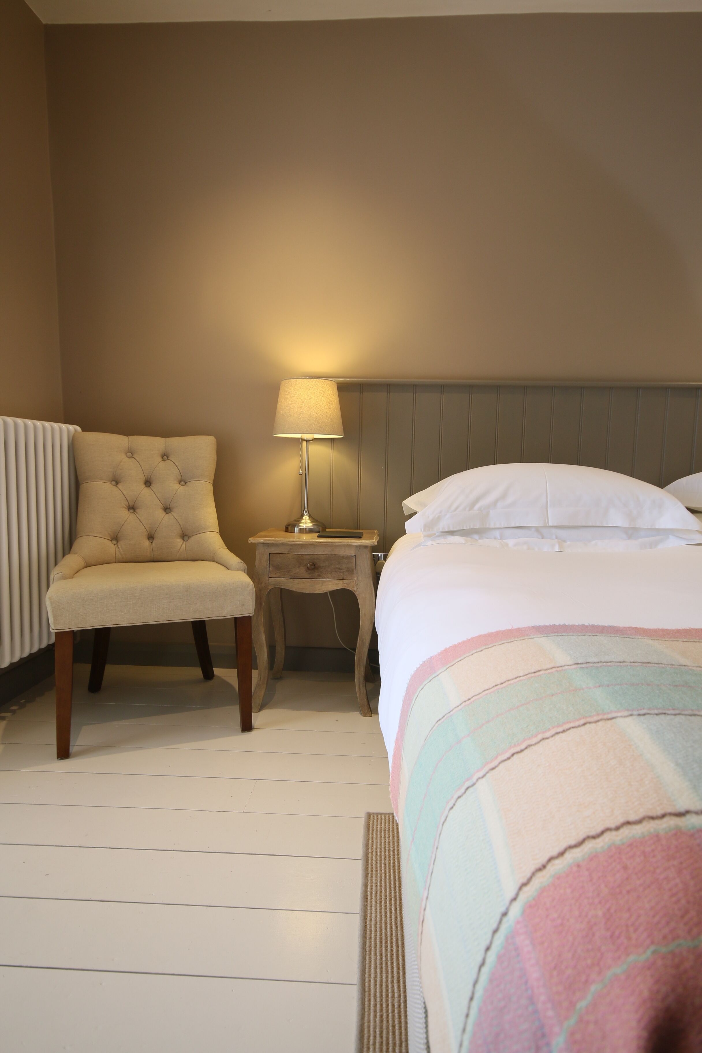 A hotel room with a bed, a chair, a nightstand, and a lamp.