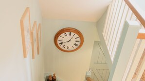 A staircase with a wooden handrail, a wall clock, and framed pictures. - The Apartments Quidhampton Mill (Salisbury)