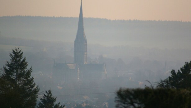 A church with a tall spire, surrounded by trees and buildings. - The Apartments Quidhampton Mill (Salisbury)